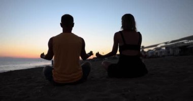 Gün doğumunda ya da gün batımında deniz kenarında yoga yapan çift. Sağlıklı yaşam tarzı ve pozitif akıl için spor konsepti