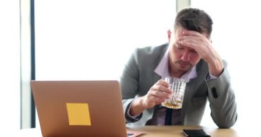 Sad depressed man holding glass of whiskey in office at workplace. Businessman alcoholic drinks alcohol