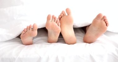 Closeup of young beautiful and loving couple playing with feet under covers. Morning awakening and waking up in morning in bed