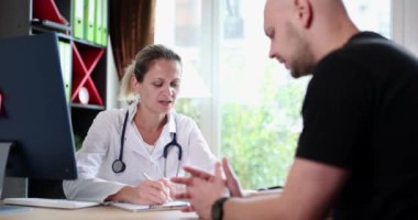 Concentrated female medical doctor giving medical consultation to man. Medic explaining health insurance benefits or treatment of illness