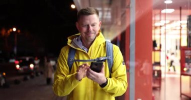 Erkek turist akıllı telefonu tutuyor ve akşam sokakta selamlaşırken elini sallıyor. Tanışmanın sevinci