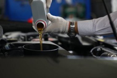 Car mechanic pours engine oil into car engine closeup. Oil change auto concept