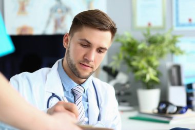 Focused doctor working in medical office signing documents brought by assistant. Health insurance and medical documents map