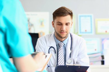 Male doctor carefully examines documents in office of clinic at workplace. Medical diagnosis and treatment prescription concept