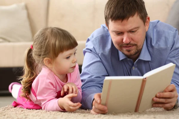 父は寝室の床に寝そべっている娘に本を読んでいる 家族の読書と時間概念の共有 — ストック写真