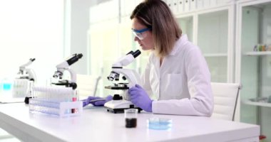 Bilimsel laboratuvar asistanı bilim adamı araştırma sonuçlarını yazıyor. Kadın mikroskoba bakar ve tıbbi analizleri inceler.