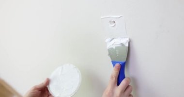 Çatlak beyaz duvarı spatulayla tamir eden bir adam. Duvarların ve açıkların onarımı