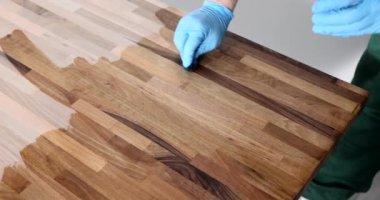 Ahşap yüzeyi koruyucu sıvı vernikle kaplayan eldivenli marangoz elleri. Mobilya cilalayan katılımcı