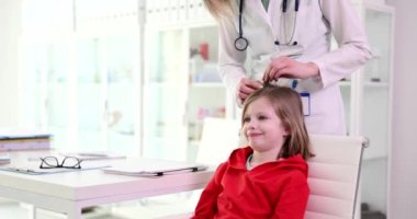 Doktor çocuk doktoru saçlarını ve klinikteki küçük kızın başını kontrol ediyor. Çocuklarda pediküloz semptomlara neden olur.