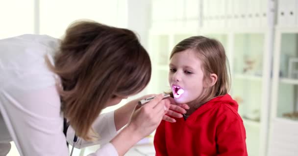 女性の耳鼻咽喉科医は 痛み症候群の患者の子供の喉に光を輝きます 小児および急性扁桃炎の大規模な扁桃体 — ストック動画