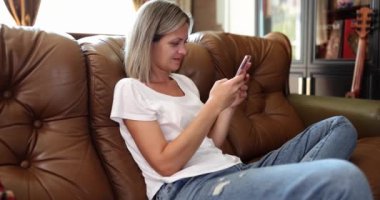 Kanepede oturan kadın akıllı telefondan mesajları dikkatlice okur. İnternet ve çevrimiçi alışveriş hakkında bilgi araması