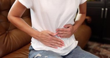 Kadın evdeki koltukta otururken şiddetli karın ağrısından muzdarip. Acı dolu dönemler tedaviye neden olur