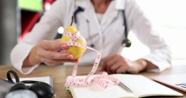 Kadın beslenme uzmanı danışmada bant ölçüsüne sarılı sarı armut tutuyor. Düzgün beslenme vitaminleri ve diyeti