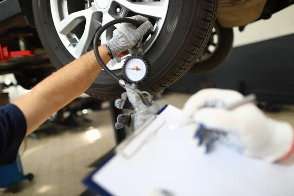 Checking tire pressure by auto mechanic in car repair shop. Tire condition monitoring concept
