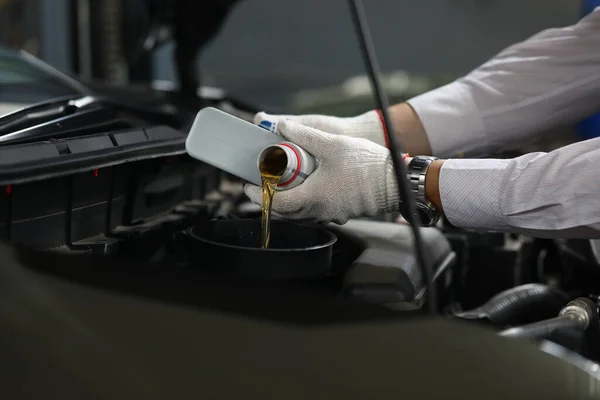 Auto mechanic pours oil into car engine from cans of oil. Oil change in car concept