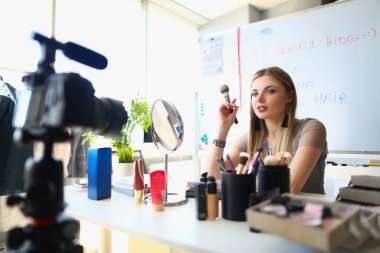 Kadın, göz farı paletli kozmetik ürünleri ve fırça fırçalarının çevrimiçi video kaydından bahsediyor. Kozmetik blogu için video çeken kadın blogcu