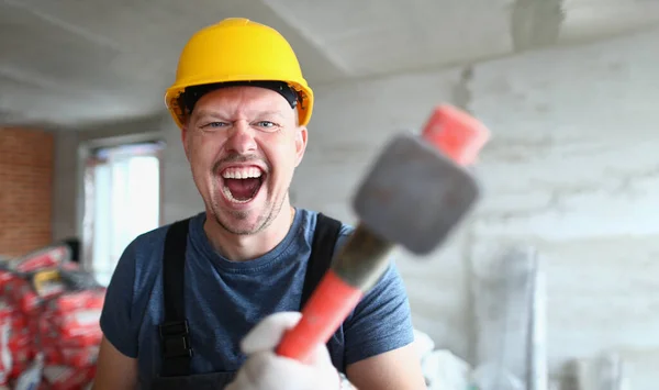Builder in helmet holds sledgehammer hammer and screams. Engineer is angry production problems and bullying in work team