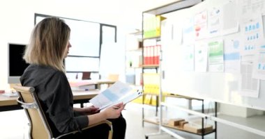 Ofisteki pazarlamacı kadın beyaz panoda analitik bilgiler üzerinde çalışıyor. Grafiklerdeki istatistik ve mali veriler