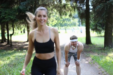 Güzel bir atlet kadın ve yorgun bir adam parkta koşuyor. Spor sağlık ve yorgunluk kavramı
