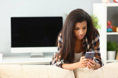 Afrikalı kadın akıllı telefon kullanarak evde sohbet ediyor. Telefon konseptinde haber okuyan siyahi kadın.