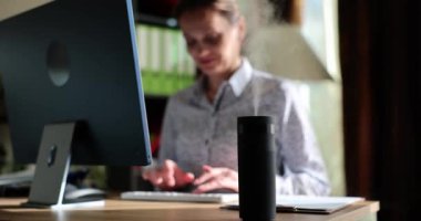 Genç bir kadın masa iyonizörünün üzerindeki bilgisayarın başında oturuyor, yakın plan. Hava temizleyici, ofis için ev aletleri.