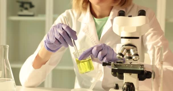 実験室のアシスタントは フラスコ クローズアップで黄色の油のサンプルを振る 燃料の品質に関する化学研究 — ストック動画
