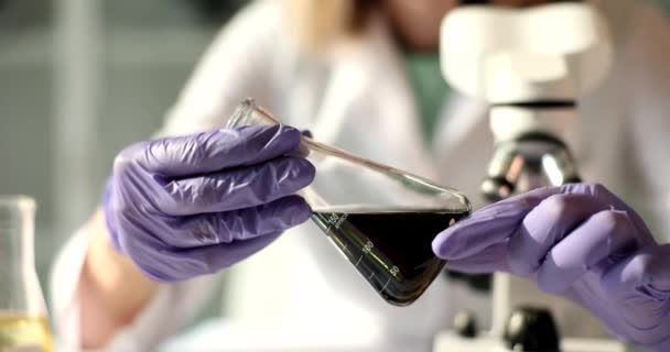 化学者は フラスコ内の黒い油のサンプルをチェックし クローズアップします 燃料品質の認証 — ストック動画