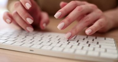 Beyaz kablosuz klavyeye manikür yapan genç bir kadın el, yakın plan. Ofis çalışanı