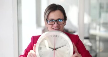 Ofisteki bir iş kadını büyük bir duvar saati tutuyor, yakın plan. Fazla mesai kavramı, son teslim tarihi