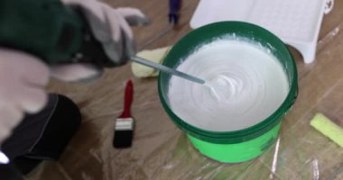 Odadaki müteahhit boyayı çırpıcıyla karıştırıp tamir ediyor. Duvara beyaz boya