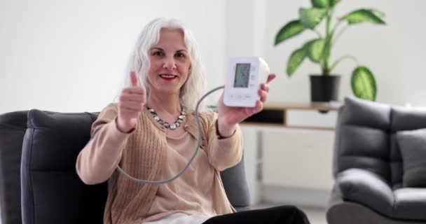 老年妇女 头发灰白 大姆指向上 血压计在家里有正常的血压4K电影慢动作 老年人动脉高压治疗的概念 — 图库视频影像