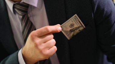 İş adamı ceketin cebinden 100 dolarlık banknot alıyor. Rüşvet kavramı