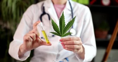 Kadın doktor elinde taze kenevir yaprağı ve elinde yağ bulunan bir tüp tutuyor. Üniformalı kadın, alternatif ilaç olarak ağır çekimde psikoaktif ilaçlar gösteriyor.