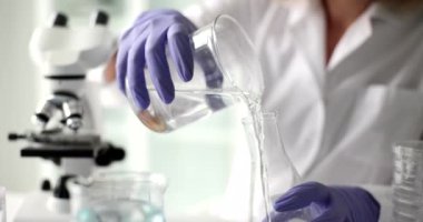 Lastik eldivenli laboratuvar çalışanı soruşturma için temiz suyu şişeye boşaltıyor. Kadın mikroskop altında ağır çekimde sıvı hazırlıyor.