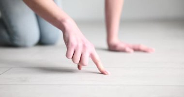 Ev hanımı lamine zeminde parmak ile toz topluyor. Kadın parmaklarını yere sürterek daireyi yavaş çekimde temizleme ihtiyacını kontrol ediyor.