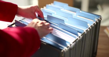Kadın, şirket arşivindeki kart indeks kutusunda dosya arıyor. Ofis çalışanı sözleşmeyi bulmak için belgeleri kontrol ediyor. Şirkette organize evrak sistemi