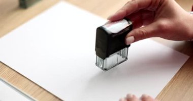 Kadın, ofisteki yavaş çekimde boş kağıtlara damga basar. Kâtip, işyerindeki resmi belgeye işaret koymuş. İstek onaylandı