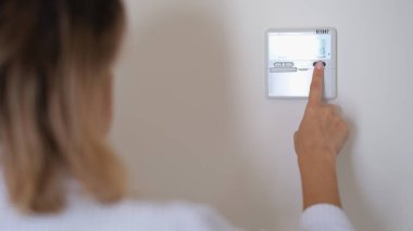 Duvardaki klimanın uzaktan kumandalı düğmesine basan kadın. Ev konseptinde konforlu sıcaklık