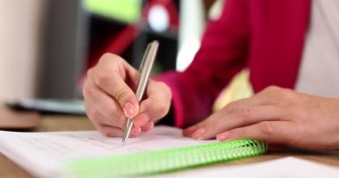 Kadın muhasebeci ofiste oturan tükenmez kalemle belgeleri imzalıyor. Pembe ceketli kadın ofiste evrak işlerini ağırdan alıyor.