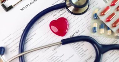 Steteskoplu kırmızı kalp oyuncağı ve haplar klinikteki hastanın tıbbi geçmişinde yatıyor. Tıbbi ekipman ve kalp hastalıkları konsepti