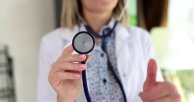 Tatmin olmuş kadın doktor elinde steteskopla baş parmağını kaldırıyor. Tıbbi üniformalı kadın, ağır çekim tıbbi ekipman operasyonunu onayladı