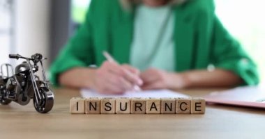 Masada potansiyel risk olarak motorsiklet modelinin yanındaki tahta küplerden yapılmış kelime sigortası. Yeşil ceketli kadın çalışan, ağır çekimde sözleşme imzaladı.