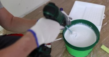 İnşaatçı, odanın zemininde elektrikli mikserle kovada sıvı boya karıştırıyor. İşçi ev bakımı için malzeme hazırlar. Ev yenilenmesi