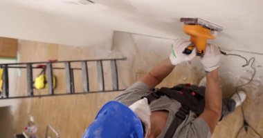 Solunum cihazlı tamirci tamir odasındaki beyaz duvarı işlemek için elektrikli cilacı kullanıyor. Çalışan, boyama için panel yüzeyi hazırlıyor. Ev bakımı