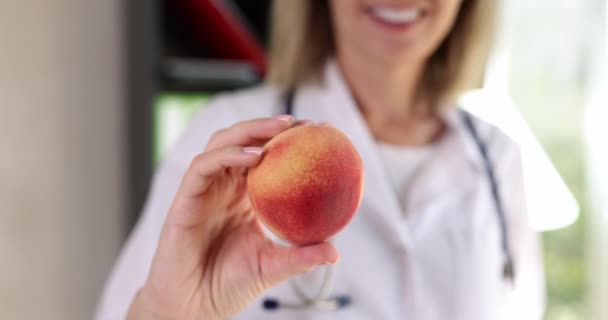 朗らかな女性医師が手を笑顔で新鮮な熟した桃を保持しています ポジティブな女性とともに果物手で健康的な食生活を承認クリニック — ストック動画
