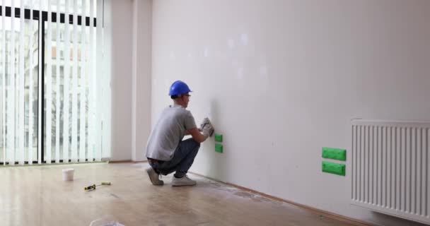 带头盔的建筑工人在翻新后的房间慢动作中 在墙上涂上石膏斑 有重点的工人用手工工具研磨干墙面板 住房的修理 — 图库视频影像