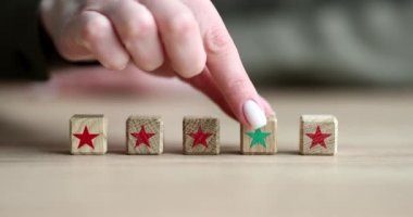 Kadının eli, kırmızı yıldızlı bloklara karşı yeşil yıldızlı tahta küp koyuyor. Liderlik kavramı ve uymama yavaş çekim