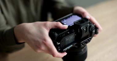 Kadın fotoğraf çekiminden önce profesyonel kamera modunu ayarlıyor. Yetenekli fotoğrafçının elleri büyük mercekli modern ekipmanları ağır çekimde tutuyor.