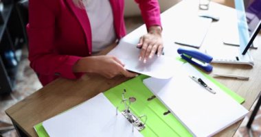 Kadın büyük klasöre koymak için küçük delikler açıyor. Pembe ceketli kadın sekreter ofiste ağır çekimde malzemelerle çalışır.