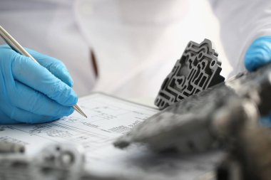 Eldivenli bilim adamı araba vites kutusu yedek parçaları üzerinde teknik araştırma yapıyor. Mühendis araştırmacısı kapakçık gövdesinin detaylarını işaretler ve detayları değerlendirir.